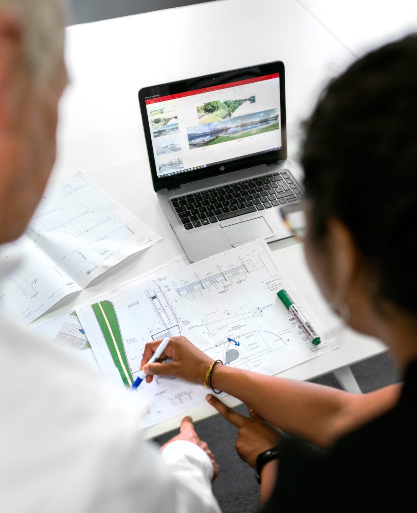 Man and woman looking at paperwork that contains graphs and comparing them to information on their laptop.