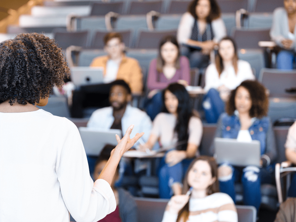 Professor in large lecture hall filled with students on their devices.