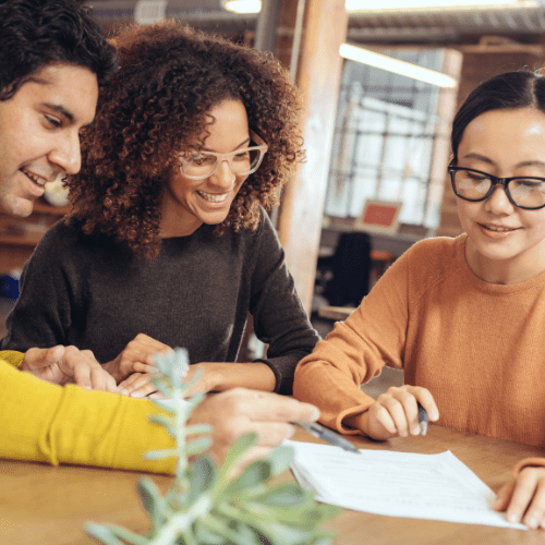 3 people sitting around a table looking at paperwork together.