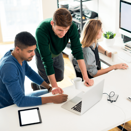 Office setting with three associates shown working on their laptops and desktop computer. A tablet and cell phone are also sitting on the desk.