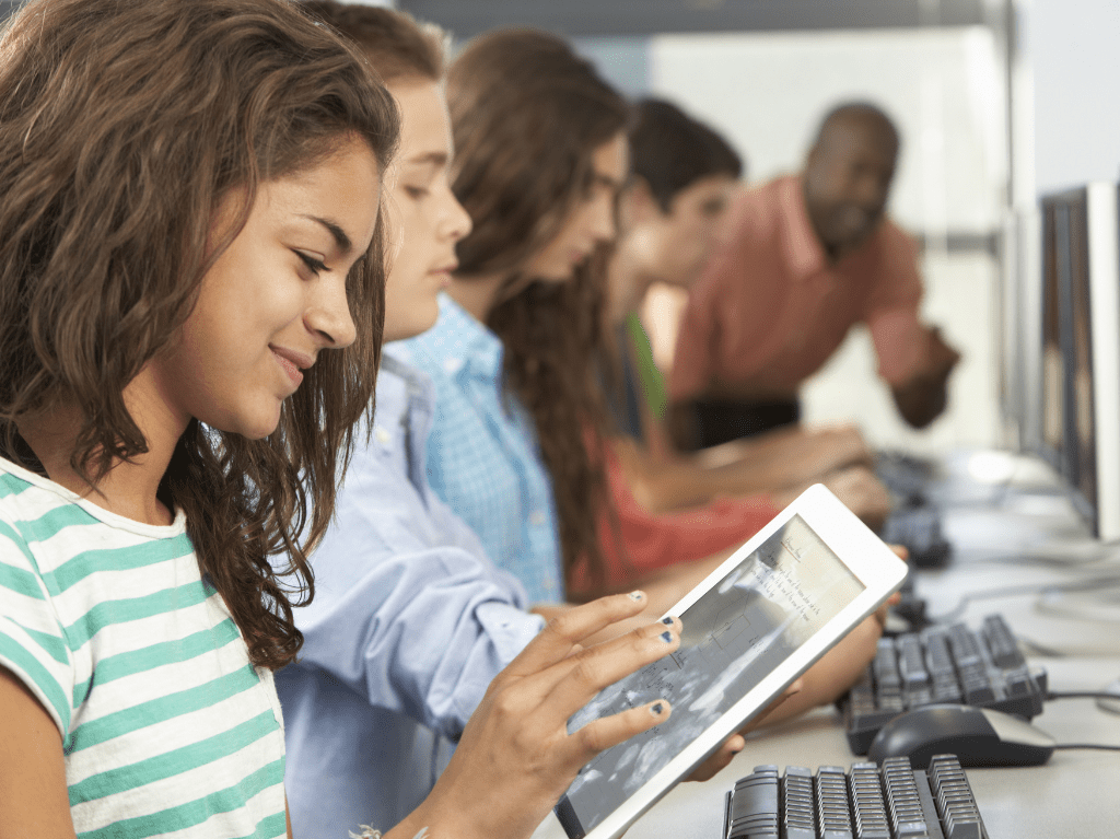 Students working on computers and tablets in a classroom.