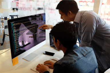 Two co-workers reviewing data on a apple computer.