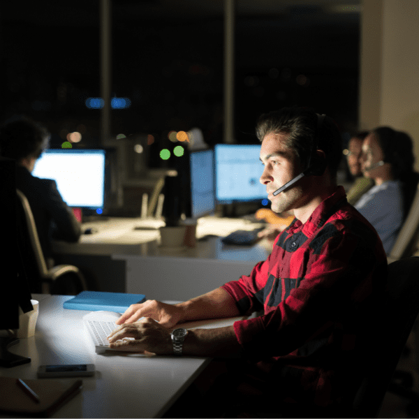 An IT Helpdesk associate working at his computer with a headset during the evening hours.